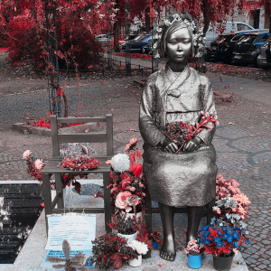 The Memorial to Comfort Women, with a woman sitting down, covered in fresh flowers with explanatory papers and plaques in front.