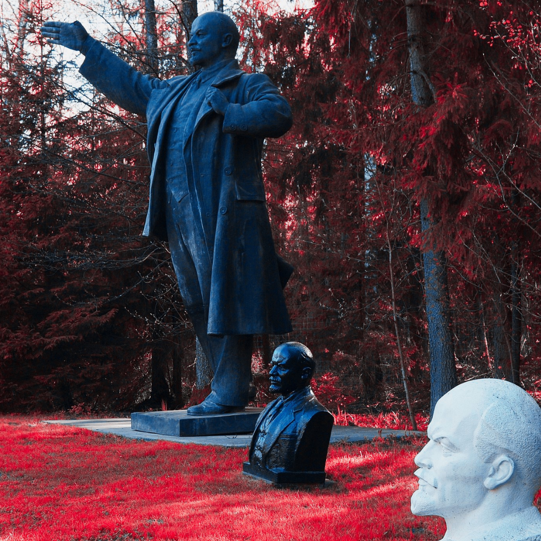 Statue of Lenin extending his hand surrounded by busts of Lenin on the ground at Grūto parkas in Lithuania