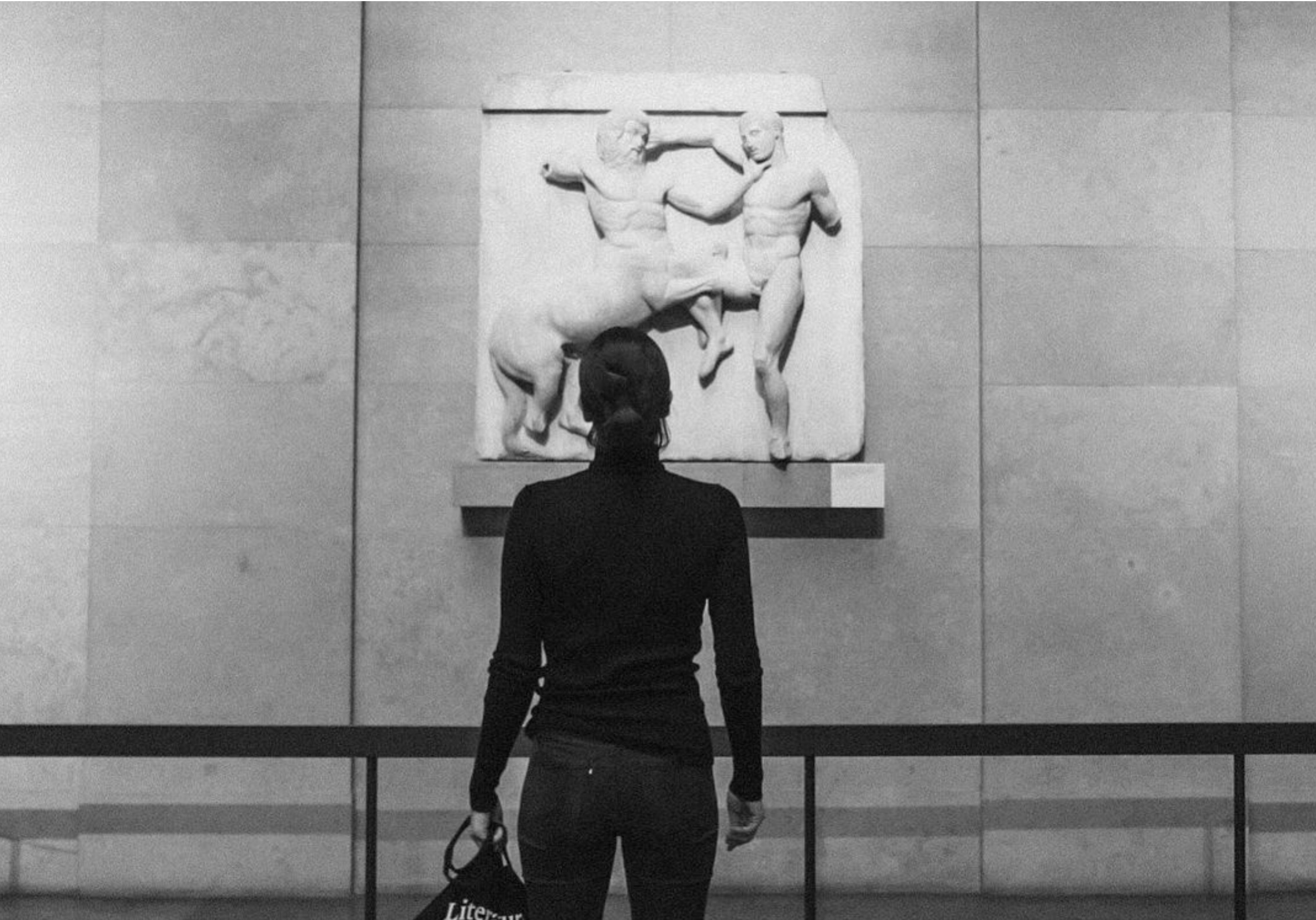 A woman stands in front of a sculpture, depicting a centaur strangling a man.